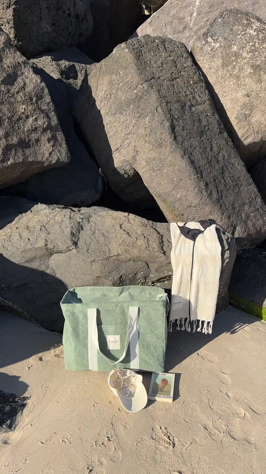 Sunday Supply Co. beach bag resting against coastal rocks on the sand