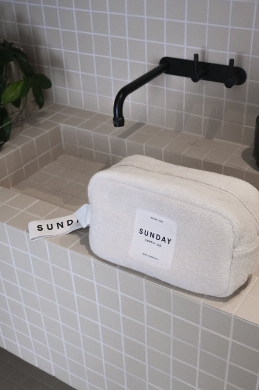 Cream towelling accessories pouch on a tiled bathroom ledge