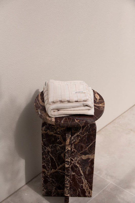 Dunes hand and face towels folded on a marble stool in a bright bathroom