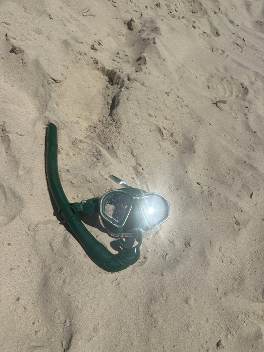 Native mask and snorkel set resting on sunlit sand after a swim