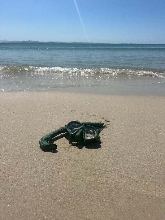Native mask and snorkel set on the sand beside clear ocean water