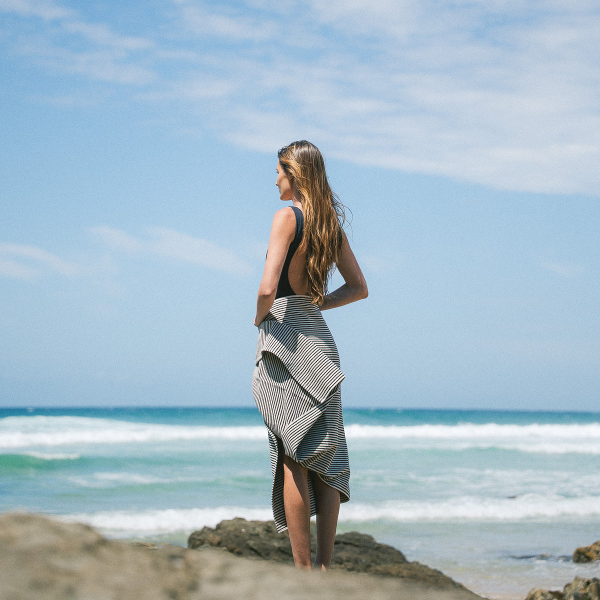 Black striped beach towel worn around the waist on a rocky beach.
