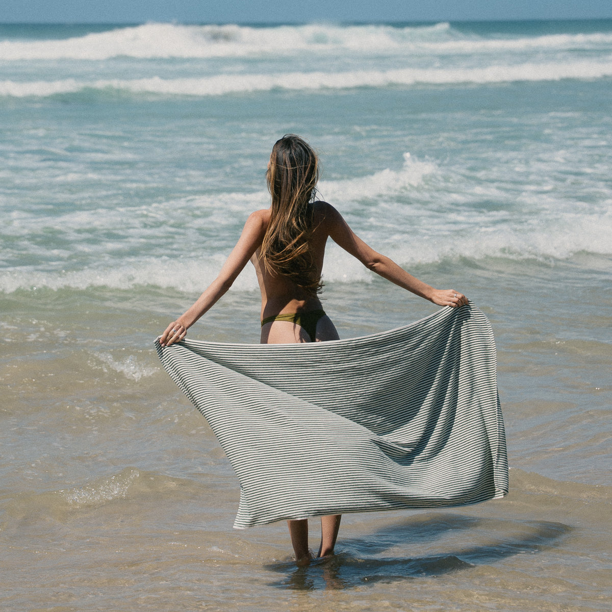 Native striped beach towel held open beside the water.
