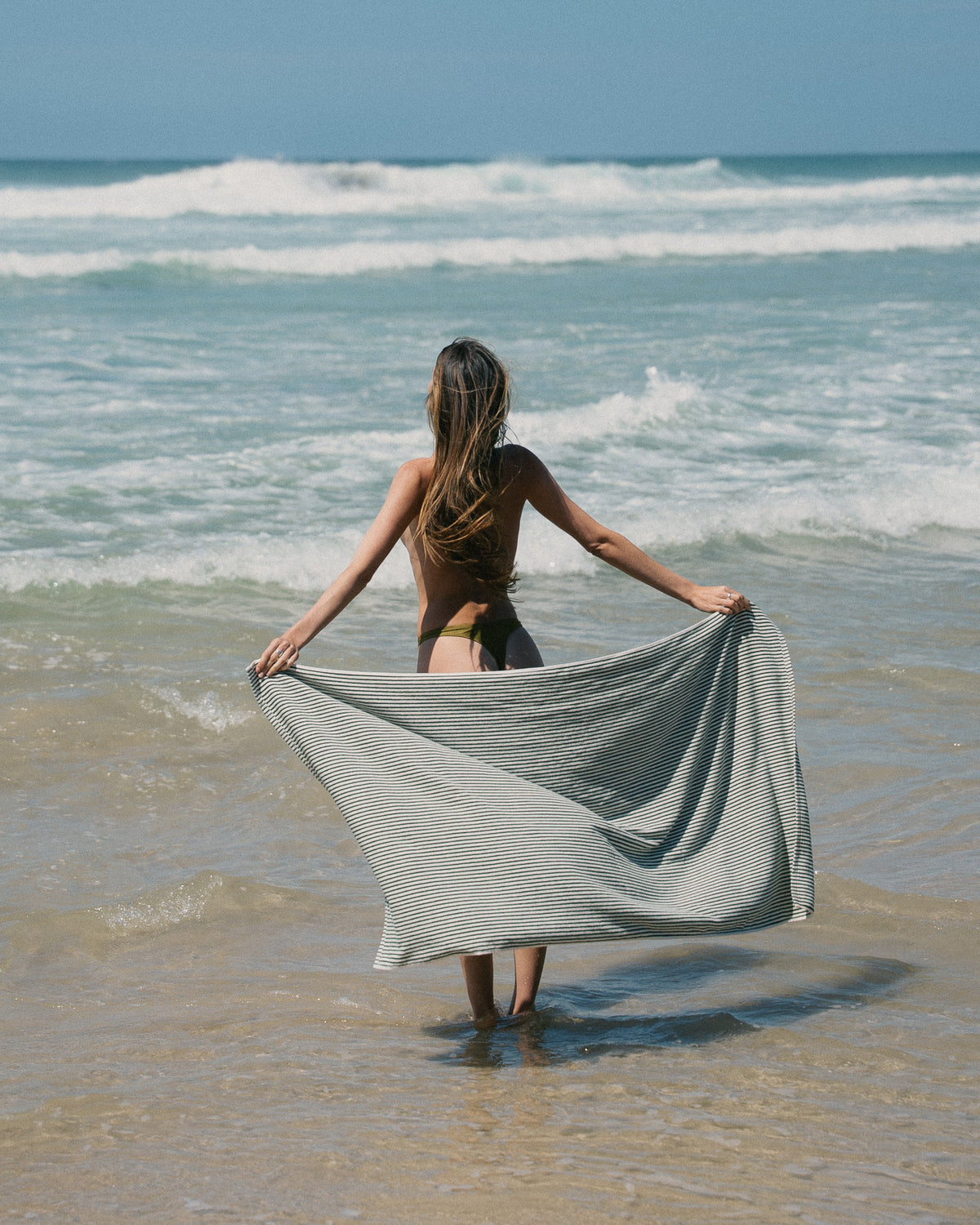Native striped beach towel held open beside the water.