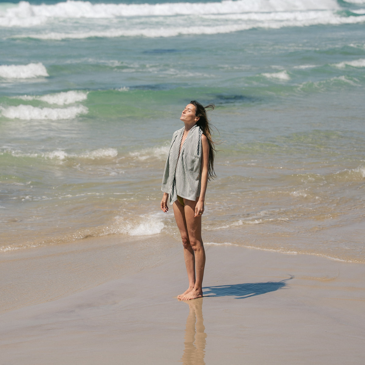 Native striped beach towel draped over a model's shoulders at the shoreline.
